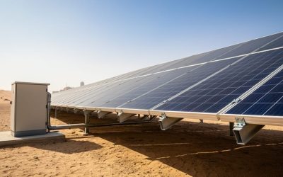 Ground-mounted solar photovoltaic panels in an Oman desert landscape under bright midday sunlight, with nearby inverter equipment and mounting structure visible.